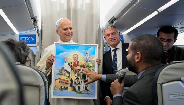 Pope Leo holds a painting gifted to him by a journalist aboard the papal plane. Photo: Vatican Media