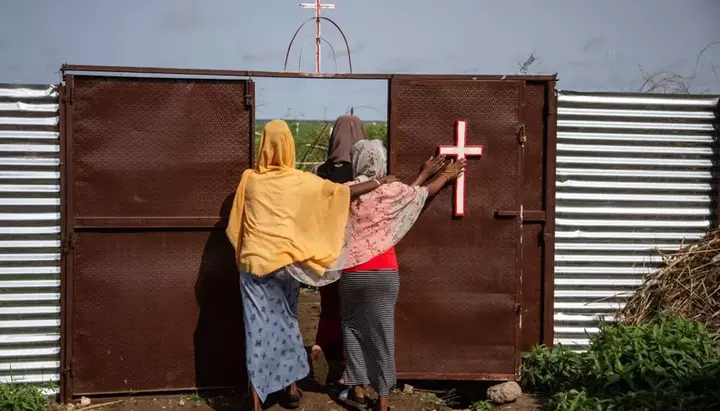 Three women touch the cross as they exit the Catholic church in the refugee camp in Shagarab, Sudan. Photo: Abdulmonam Eassa/Getty Images